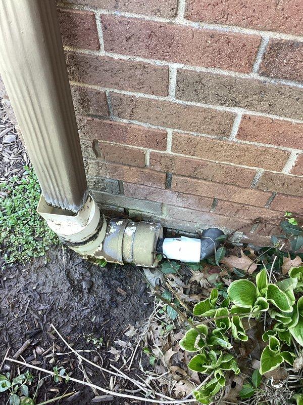 Performed camera inspection of exterior ABS drainage line at foundation level. Documented downspout connection point and horizontal drain pipe assembly where weathered PVC coupling joins corrugated metal downspout to underground drainage system. Identified repair location at base of building where foundation drainage requires attention due to compromised pipe connections in landscaped area.