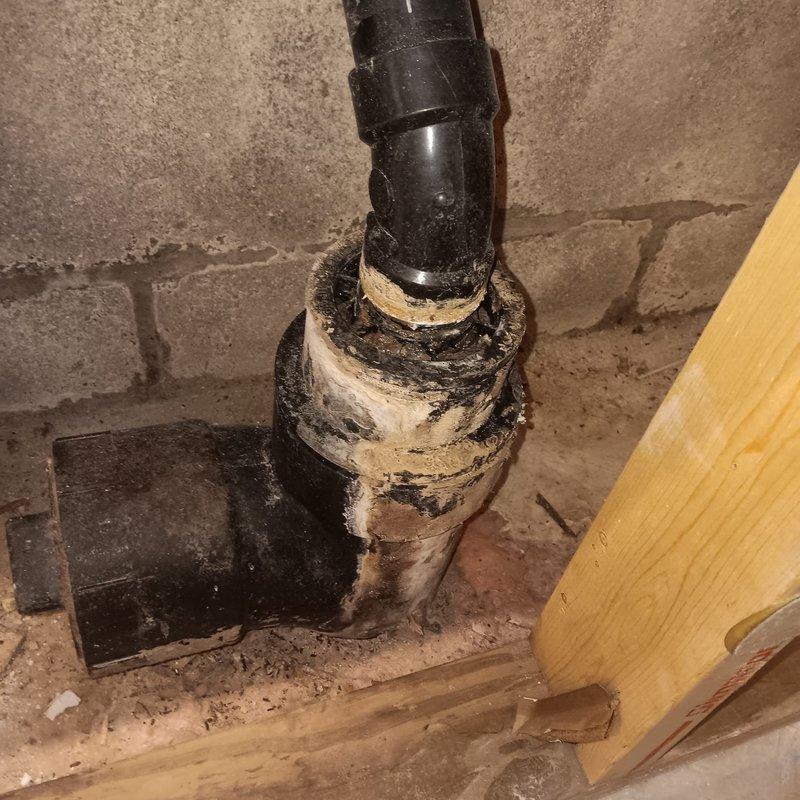 Conducted diagnostic evaluation of residential sewer line experiencing recurring backup issues. Assessed existing plumbing infrastructure in basement utility area, including vertical drain stack and floor-level sewer connections. Documented deteriorated condition of existing piping system, noting severely degraded paint, corrosion, and wear on junction components where vertical stack meets floor penetration. Identified aging cast iron or clay piping system requiring backwater valve installation to prevent sewage backflow into property. Photographed current plumbing configuration and condition of concrete floor penetrations and wall-mounted drainage components to develop installation plan for backwater valve assembly.