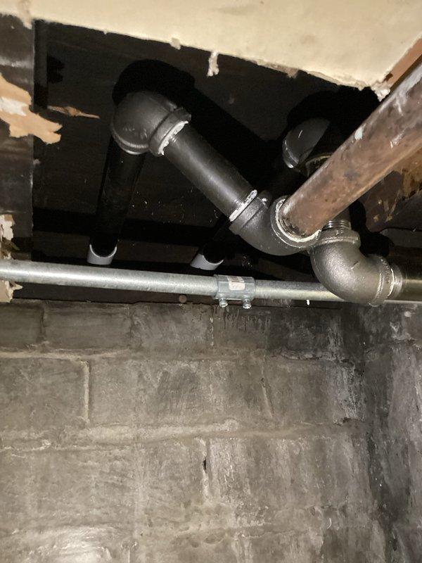 Completed gas meter relocation from exterior wall mounting to new position. Relocated two large capacity gas meters with associated supply piping, reconfigured gray piping network with new vertical and horizontal runs secured with wall-mounted brackets, and installed necessary elbows and T-joints to ensure proper gas flow to building. Modified interior basement piping connections including black steel and galvanized pipe sections with proper fittings and support clamps to accommodate the meter repositioning while maintaining code compliance and system integrity.