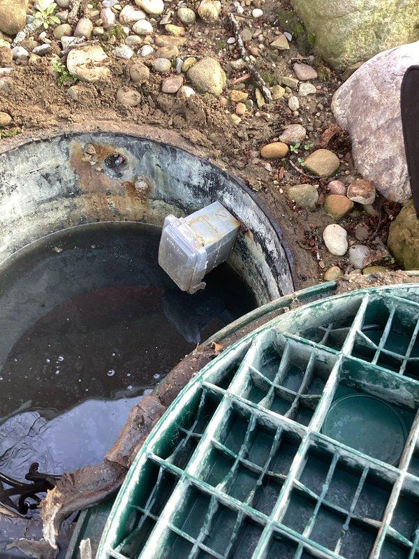 Responded to service call for circuit breaker repeatedly tripping on septic pump system. Upon arrival, inspected outdoor septic sump basin and associated electrical components. Found submersible pump in concrete basin with visible signs of system age and weathering. Assessed pump operation, float switch functionality, and electrical connections at outdoor utility area near meter assembly. Evaluated PVC discharge piping system and verified proper drainage configuration. Documented existing conditions showing stagnant water levels, pump positioning, and overall system setup including white float device and plumbing connections along exterior wall. Performed diagnostic testing to determine root cause of electrical overload condition affecting dedicated pump circuit.