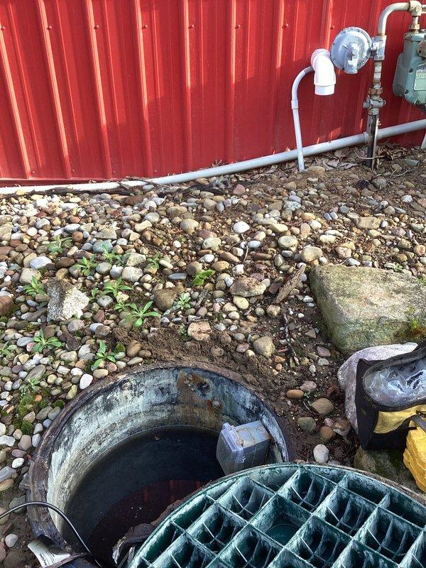 Responded to service call for circuit breaker repeatedly tripping on septic pump system. Upon arrival, inspected outdoor septic sump basin and associated electrical components. Found submersible pump in concrete basin with visible signs of system age and weathering. Assessed pump operation, float switch functionality, and electrical connections at outdoor utility area near meter assembly. Evaluated PVC discharge piping system and verified proper drainage configuration. Documented existing conditions showing stagnant water levels, pump positioning, and overall system setup including white float device and plumbing connections along exterior wall. Performed diagnostic testing to determine root cause of electrical overload condition affecting dedicated pump circuit.
