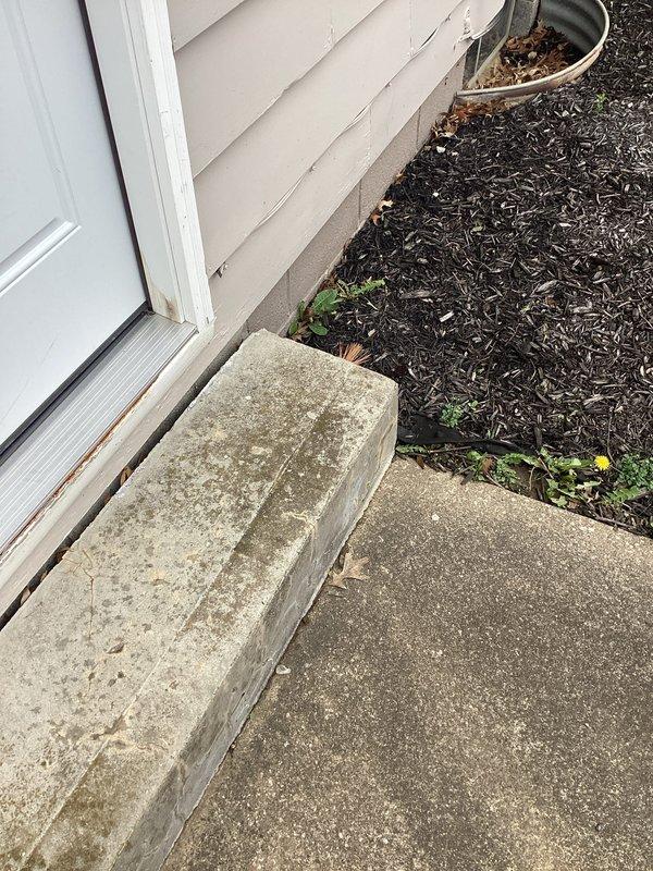 Responded to basement water intrusion complaint following recent downspout replacement. Upon inspection, identified sump pump system and drainage access point in basement floor area. Exterior assessment revealed potential water infiltration points at door threshold and foundation perimeter where landscaping meets concrete surfaces, with visible moisture staining and organic growth indicating ongoing water exposure. Documented existing conditions of sump pump cover with temporary sealing measures and drainage hose configuration for follow-up service scheduled.