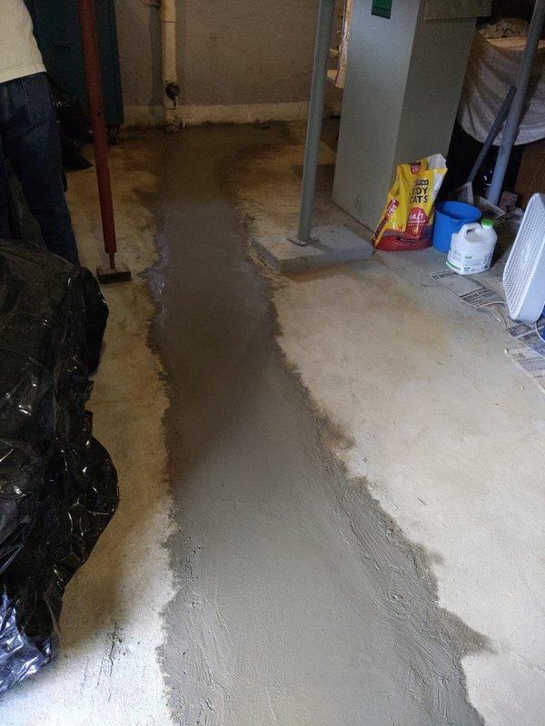 Completed comprehensive assessment of basement main drain system experiencing significant water damage and moisture infiltration. Documented extensive floor staining and discoloration patterns indicating chronic drainage issues. Photographed existing plumbing configuration including vertical drain pipe, valve connections, and areas of water accumulation to provide detailed estimate for main drain line replacement and waterproofing solutions.