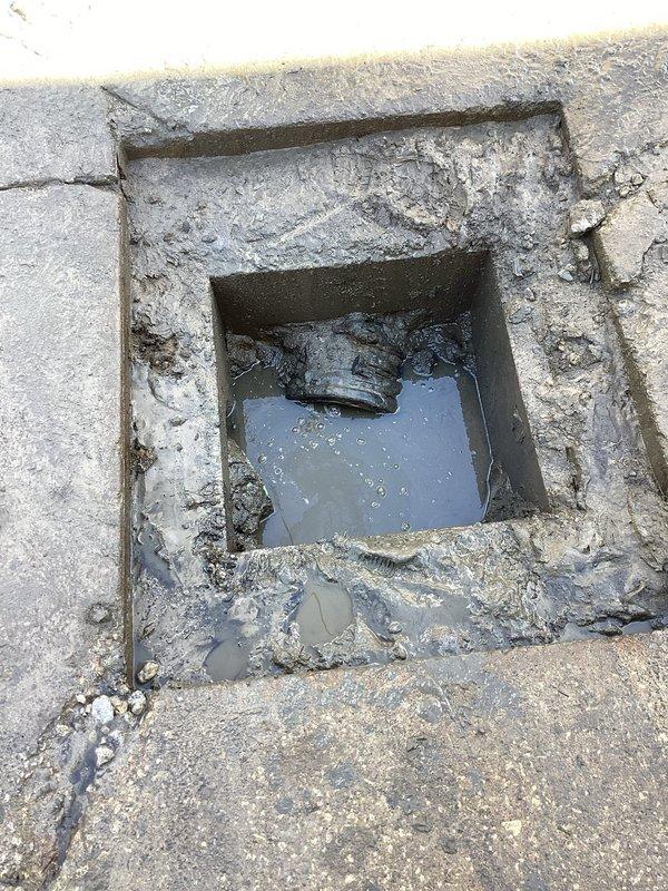 Responded to service call for ground water drainage assessment at commercial property. Upon arrival, checked in at office as requested and proceeded to inspect the exterior drainage system located on the side of the building. 

Performed diagnostic evaluation of existing floor drain installed in concrete pavement. Found drain cavity containing significant standing water with murky appearance, indicating inadequate drainage capacity or potential blockage in downstream piping. Observed weathered concrete frame surrounding drain opening with visible structural deterioration including multiple cracks, chips, and surface degradation. Noted accumulation of debris and sediment within drain opening and around perimeter, partially obstructing flow. Dark drainage component visible within cavity but submerged conditions prevented full assessment of internal mechanism functionality.

Documented extensive cracking in surrounding pavement radiating outward from drain location, suggesting possible se