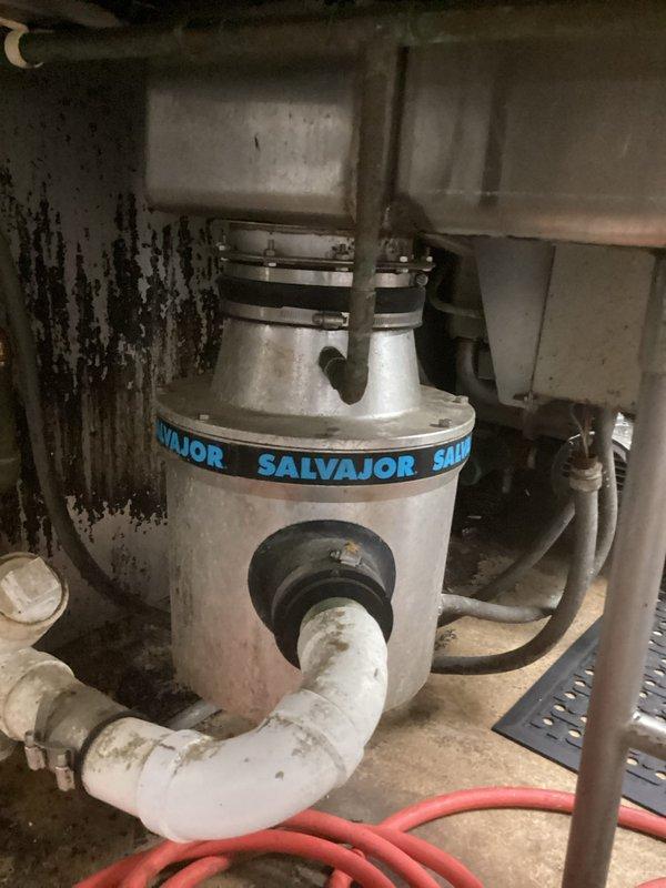 Responded to service call for non-operational commercial garbage disposal unit. Upon inspection, identified Salvajor Model 300 disposal system installed under commercial sink with visible signs of wear and operational failure. Assessed unit condition, documented equipment specifications and installation configuration, and photographed disposal assembly including mounting, drainage connections, and electrical components for service records and future reference.