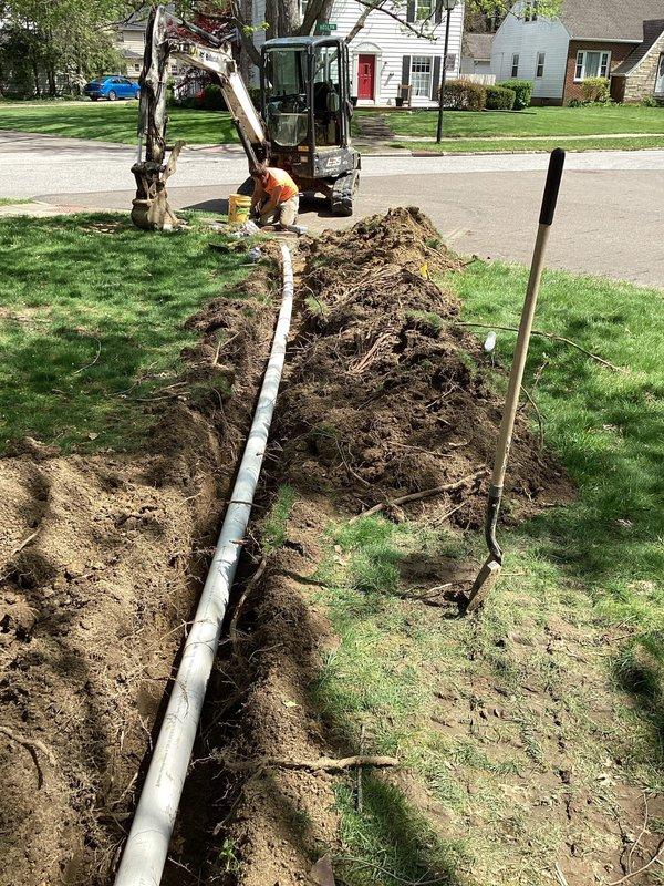 Installed approximately 60 feet of Schedule 35 PVC drainage pipe from the rear left corner of the residence to the street, terminating with a pop-up emitter. Excavated trench through front lawn to accommodate new drainage line. Modified existing sump pump discharge by cutting the 1-1/2" line after the existing 90-degree elbow, installed additional 90-degree fitting, and redirected discharge into a dedicated 4" riser for improved drainage performance. Backfilled trench upon completion of installation.