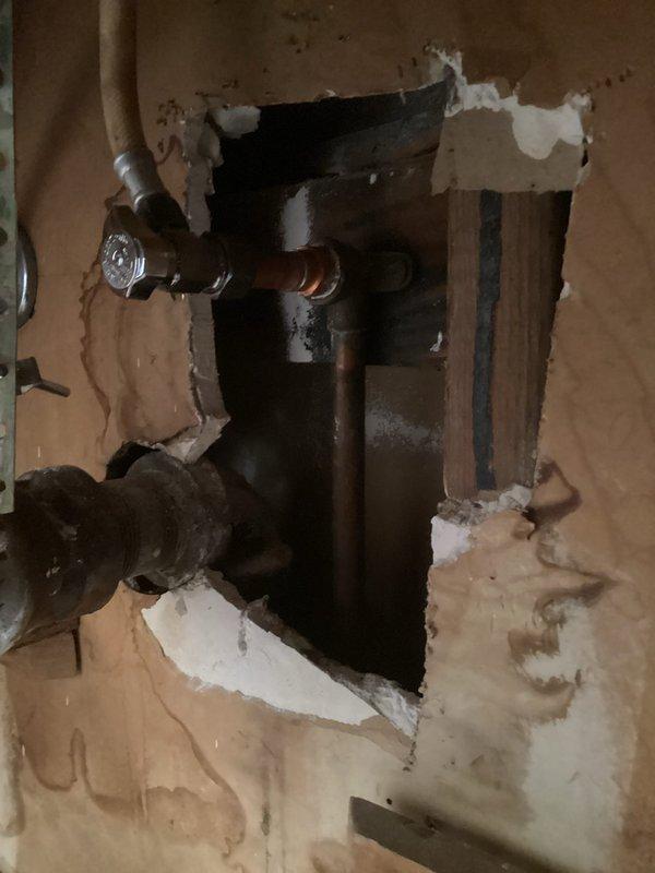 # Plumbing Service Completed

Responded to service call for suspected gas leak originating from HVAC system in residential property constructed in 1964. Upon arrival, conducted thorough inspection of mechanical systems in basement/crawl space area and accessed plumbing behind interior wall. 

Inspection revealed aging brass and copper piping with threaded connections showing signs of corrosion and surface discoloration consistent with original 1964 installation. Examined valve assembly with brass fittings and multiple pipe segments with threaded couplings supported by foam pipe insulation. Created wall access point to expose concealed plumbing system for comprehensive evaluation of pipe conditions and connections.

Assessed horizontal pipe runs with valves and connectors for potential leak sources. Evaluated condition of all visible joints, fittings, and connections throughout the plumbing system. Inspected interface between plumbing components and HVAC ductwork to identify potential g