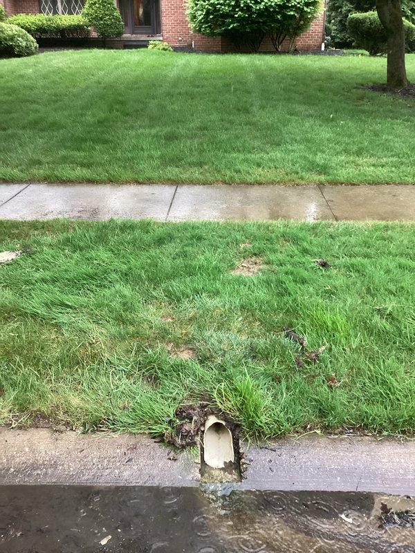 Responded to drainage issue at approximately 40-year-old residence on second scheduled visit. Upon arrival, assessed exterior drainage system and identified water flow from curb drainage pipe opening onto street pavement. Inspected residential plumbing drainage infrastructure and cleared obstruction causing backup in main drain line. Verified proper water flow through system and confirmed drainage issue resolved. Property exterior showed normal water discharge through curb outlet following service completion.