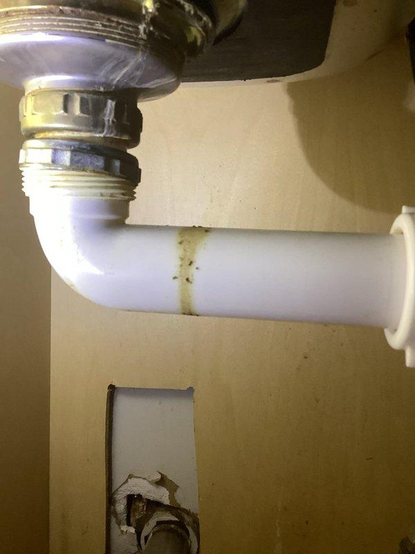 Responded to multiple plumbing leaks including toilet leak penetrating ceiling, kitchen sink leak, and bathroom sink leak. Inspected toilet seal and wax ring for source of water intrusion causing ceiling damage. Examined kitchen sink drain assembly and P-trap, noting discoloration and residue buildup on PVC components indicating previous leak activity. Assessed drain connections, compression fittings, and trap assembly for proper sealing. Inspected bathroom sink plumbing fixtures and drain components. Addressed all leak sources to prevent further water damage and restore proper drainage function throughout affected areas.
