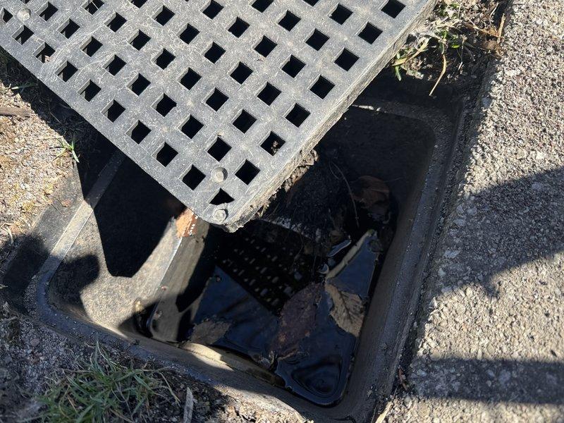 Responded to service call regarding ground water drain concerns and driveway subsidence. Inspected utility access vault with latticed metal grate, documenting existing drainage infrastructure including visible piping, valve assemblies, and connection components within the recessed cavity. Assessed driveway conditions where concrete sections showed signs of settlement and sinking, marking affected areas for reference. Examined grate stability issues where current cover design allows displacement during water flow events. Recommended drain line inspection for potential blockages and evaluation of underground drainage system integrity to determine if compromised piping is contributing to driveway settlement. Advised consideration of alternative grate design with secured mounting to prevent flotation during high water flow conditions.