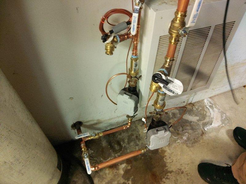 Completed replumbing of water meter and deduct meter assembly in commercial utility space. Installed new copper piping with brass fittings and shutoff valves, replaced mounting brackets and pipe supports, and pressure-tested system to ensure proper operation. Addressed previous moisture damage area on concrete floor surrounding the plumbing infrastructure.
