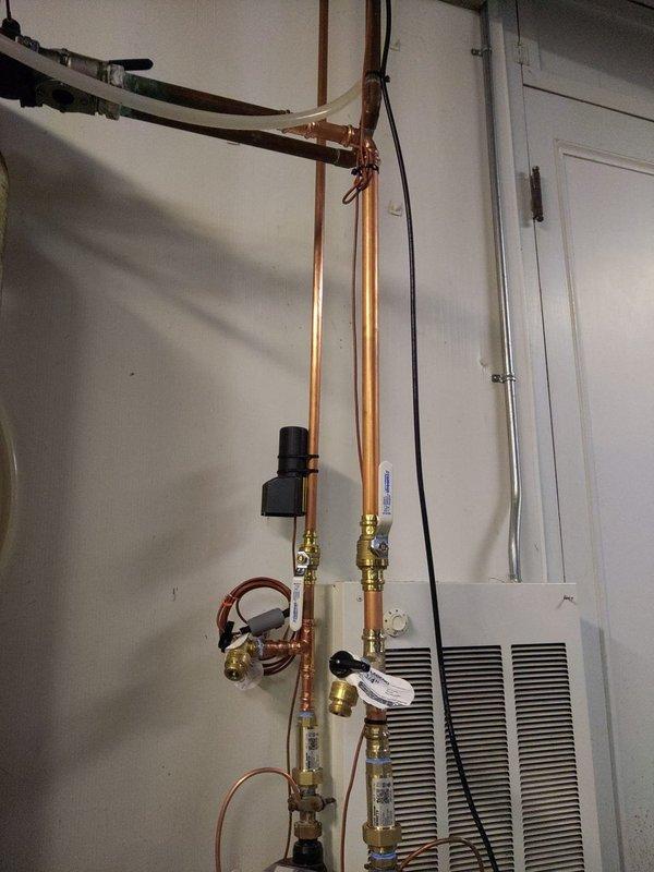 Completed replumbing of water meter and deduct meter assembly in commercial utility space. Installed new copper piping with brass fittings and shutoff valves, replaced mounting brackets and pipe supports, and pressure-tested system to ensure proper operation. Addressed previous moisture damage area on concrete floor surrounding the plumbing infrastructure.