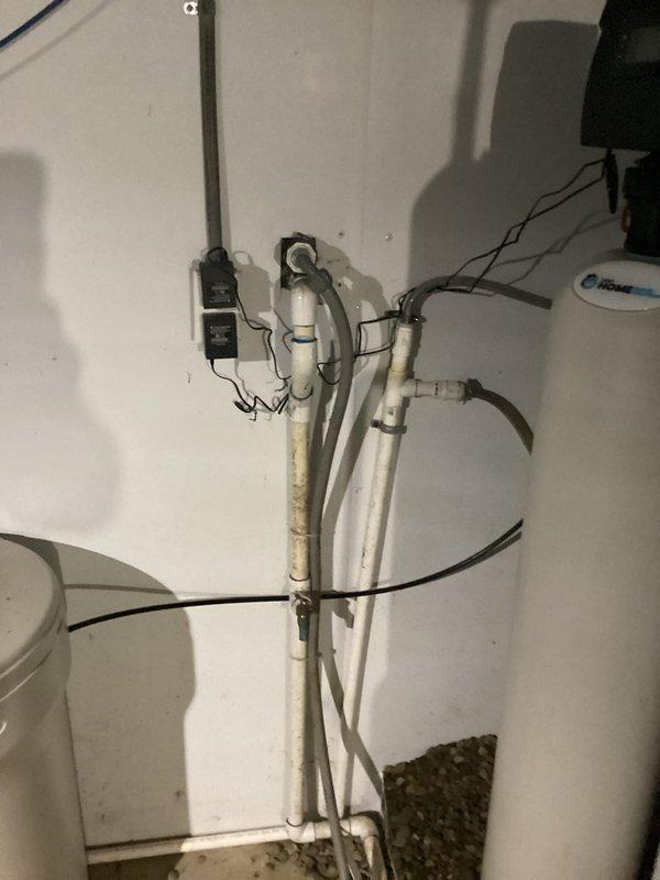 Responded to water leak investigation at a 70-year-old residential property where the homeowner suspected a leak originating from the well system. Conducted thorough inspection of exterior grounds near the foundation, identifying dark staining and moisture accumulation on concrete surfaces adjacent to the structure. Inspected interior plumbing infrastructure in the basement utility area, examining vertical pipe runs, PVC supply lines, and connections near the water heater to rule out interior sources. Documented findings with photographic evidence of both exterior ground conditions and interior plumbing configuration for further evaluation and repair recommendations.