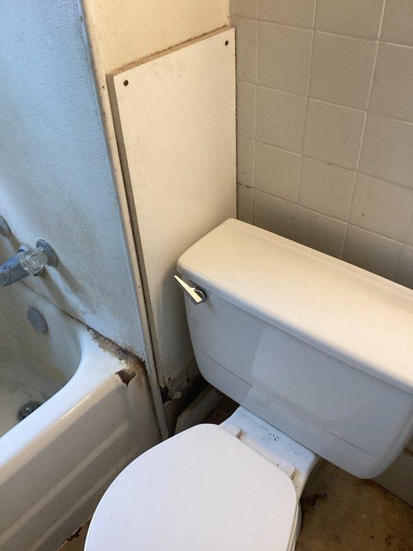 Installed customer-supplied shower valve in bathroom. The three-piece wall-mounted assembly includes a center spout and two side control valves with ceramic handles, all mounted to the tub surround wall above the bathtub fixture.