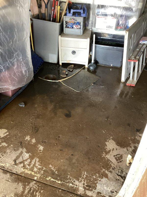 Responded to emergency call for basement flooding caused by main drain backup. Upon arrival, found significant standing water throughout basement storage area with muddy sediment covering entire floor surface. Accessed garage floor drain cleanout and performed large-capacity drain snaking procedure to clear main line obstruction. Successfully removed blockage and restored proper drainage flow. Verified system functionality and confirmed water began receding from affected area. Documented pre-existing flood damage to basement contents including furniture, storage containers, and various household items. Photographed flooded conditions and exposed basement infrastructure including plumbing lines, HVAC ductwork, and spray foam insulation applications on overhead systems.