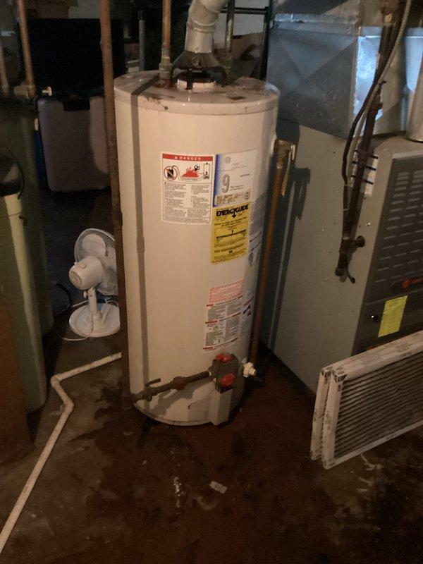 Responded to service call for leaking and corroded tanked water heater in century-old residential property. Upon inspection, confirmed active water leak with visible corrosion on tank exterior and moisture staining on concrete floor surrounding unit base. Documented existing conditions including deteriorated tank integrity, plumbing connections at top of unit, and safety valve configuration. Photographed water heater showing manufacturer specifications, energy guide labels, and safety warnings for record purposes. Advised property owner of tank failure and recommended immediate replacement due to age-related corrosion and active leak posing risk of water damage and potential catastrophic tank failure.