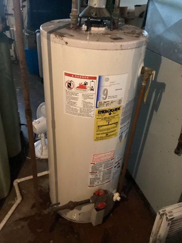 Responded to service call for leaking and corroded tanked water heater in century-old residential property. Upon inspection, confirmed active water leak with visible corrosion on tank exterior and moisture staining on concrete floor surrounding unit base. Documented existing conditions including deteriorated tank integrity, plumbing connections at top of unit, and safety valve configuration. Photographed water heater showing manufacturer specifications, energy guide labels, and safety warnings for record purposes. Advised property owner of tank failure and recommended immediate replacement due to age-related corrosion and active leak posing risk of water damage and potential catastrophic tank failure.