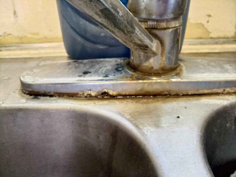 Responded to callback for leaking kitchen sink basket strainer and outlet following previous repair. Upon inspection, identified failed seal at basket strainer assembly with visible water accumulation and mineral deposit buildup around faucet base and mounting surfaces. Re-secured basket strainer with proper plumber's putty application, tightened retaining components, and verified outlet connections for proper sealing and drainage function.