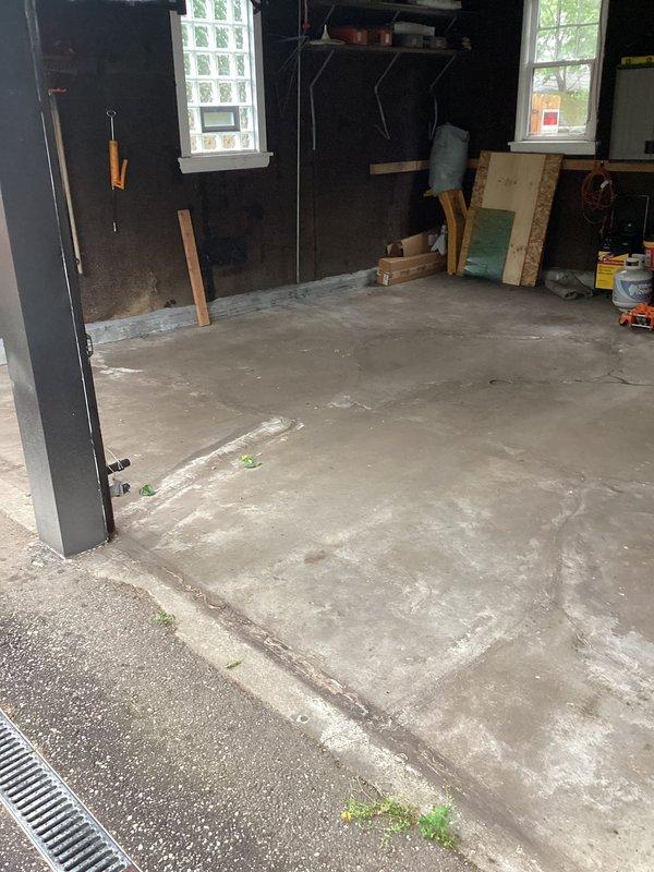 Responded to drainage issue where water from clogged garage floor drain was leaking into basement through an existing structural opening between the two spaces. Performed diagnostic assessment of the garage drainage system, identifying blockage in the linear drain grate located at the garage entrance. Documented conditions of concrete surfaces showing weathering, vegetation growth in cracks, and water intrusion pathways. Inspection revealed the garage floor drain required clearing to prevent continued water accumulation and subsequent basement infiltration through the compromised barrier between levels.