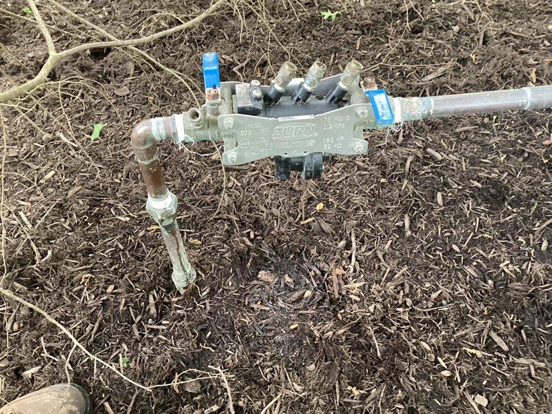 Responded to service call for cracked backflow prevention device on irrigation system. Upon arrival, inspected 1" Wilkins 375 backflow preventer (Serial# B152990) located in front left corner near street that had been previously shut off to prevent water leakage. Replaced damaged backflow assembly with new unit, reconnected white PVC supply lines and blue distribution piping to manifold assembly. Performed complete backflow test per industry standards to verify proper check valve operation and system integrity. Restored water supply to sprinkler system and confirmed no leaks at connections.