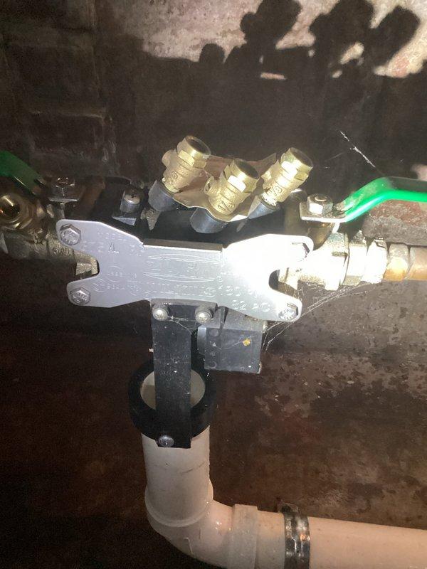 Responded to water leak in basement of 33-year-old home. Upon inspection, identified compromised backflow prevention valve assembly with brass fittings showing signs of age-related deterioration and moisture intrusion. The concrete block walls exhibited extensive water staining and discoloration, indicating chronic moisture issues. Assessed the vertical blue PVC supply line connection to the brass valve mechanism and horizontal white PVC drainage system. The copper pipe segment below the valve assembly showed corrosion consistent with prolonged water exposure. Floor surfaces displayed significant water damage and staining patterns suggesting active or recent leakage. Documented existing plumbing configuration including backflow preventer, manifold connections, and associated piping systems. Recommended valve replacement and evaluation of drainage system to prevent future water intrusion in the basement utility area.