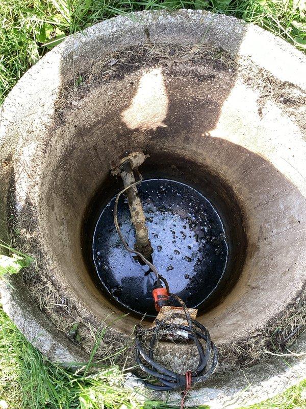 Responded to service call for wet, soggy yard conditions localized around exterior septic pump area. Upon inspection, accessed septic pump pit and found submersible pump operational with standing water present at bottom of concrete access shaft. Photographed pump installation showing power cables and discharge piping in place. Concrete structure displayed normal aging with mineral deposits and efflorescence on walls. Pump appeared to be functioning, though surface water saturation in surrounding yard indicated possible discharge line issue, pump cycling problem, or system capacity concern requiring further evaluation.