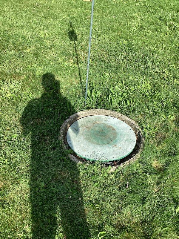 Responded to service call for wet, soggy yard conditions localized around exterior septic pump area. Upon inspection, accessed septic pump pit and found submersible pump operational with standing water present at bottom of concrete access shaft. Photographed pump installation showing power cables and discharge piping in place. Concrete structure displayed normal aging with mineral deposits and efflorescence on walls. Pump appeared to be functioning, though surface water saturation in surrounding yard indicated possible discharge line issue, pump cycling problem, or system capacity concern requiring further evaluation.