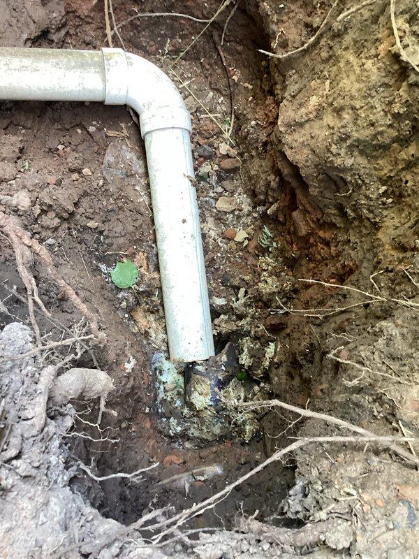 Responded to service call for disconnected sewer drain piping exiting the side of the house. Upon arrival, excavated and exposed the main line where white PVC pipe sections had become separated. Reconnected the pipes using proper coupling fittings to restore the 90-degree elbow joint configuration, ensuring secure connection between horizontal and vertical pipe sections. Verified proper alignment and functionality of the repaired sewer drain system.