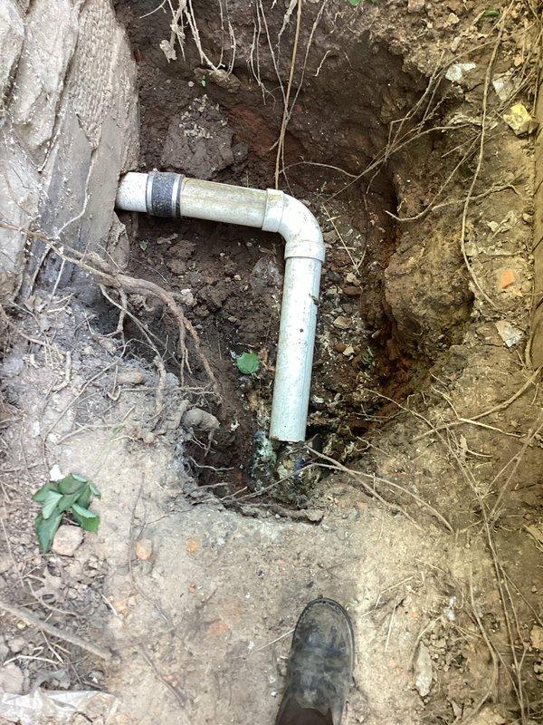 Responded to service call for disconnected sewer drain piping exiting the side of the house. Upon arrival, excavated and exposed the main line where white PVC pipe sections had become separated. Reconnected the pipes using proper coupling fittings to restore the 90-degree elbow joint configuration, ensuring secure connection between horizontal and vertical pipe sections. Verified proper alignment and functionality of the repaired sewer drain system.