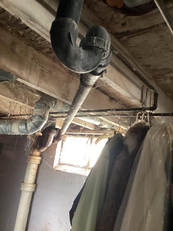 Conducted free estimate for multiple plumbing issues including a bathtub drain leaking into the basement with slow drainage despite previous snaking attempts, and a kitchen sink with an active leak underneath in the cabinet area. Performed visual inspection of basement plumbing infrastructure, documenting exposed drain lines, P-trap assemblies, and PVC piping systems beneath kitchen and bathroom fixtures. Identified water staining on basement walls and ceiling joists indicating ongoing moisture intrusion from upper-level plumbing fixtures. Photographed existing plumbing configuration including drain trap connections, pipe routing through floor joists, and areas of concern for proper assessment and estimate preparation.