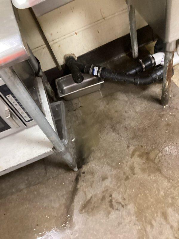 Performed camera inspection and jetting service on commercial kitchen drain line serving sandwich preparation station experiencing backup issues when sink was drained. Conducted video inspection to identify blockage location and condition of drain line, followed by hydro-jetting to clear obstruction and restore proper drainage flow. Documented equipment conditions and water damage present in affected areas, with visible moisture and staining observed on flooring surfaces near HVAC equipment and cabinet installations.