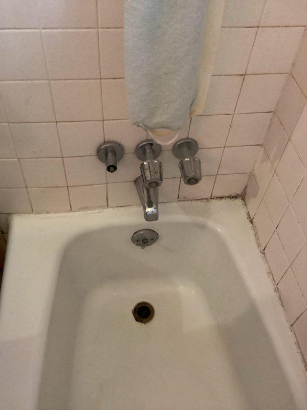 Responded to water leak originating from unit above, causing ceiling damage above bathroom shower area. Conducted assessment of affected ceiling with exposed drywall damage and inspected bathroom fixtures including three-handle tub faucet assembly. Documented extensive ceiling deterioration with compromised drywall material and photographed bathroom plumbing fixtures showing age-related wear, grout discoloration, and potential moisture infiltration points. Provided assessment and estimate for faucet repair to property management while noting priority need to address source leak from upper unit.