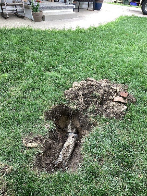 Responded to service call for clogged downspout causing water drainage issues into yard and basement. Upon arrival, performed diagnostic assessment and located underground drainage system failure. Excavated affected areas of lawn to expose buried corrugated drainage pipe and compromised downspout connection. Identified blockage and improper drainage routing causing water to pool in yard and infiltrate basement area. Cleared obstruction from drainage line, verified proper flow, and ensured downspout system was redirected to discharge water away from foundation and living spaces. Backfilled excavated areas and restored lawn surface to original condition.