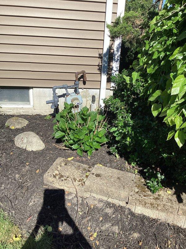 Responded to service call regarding downspout overflow and erosion issues at residential property. Conducted comprehensive inspection of entire ground water drainage system from building to street connection. Evaluated all downspout discharge points and traced underground drainage lines along side yard walkway. Inspection revealed PVC drainage piping system with multiple elbow joints near foundation, with potential blockage or inadequate slope causing water backup and overflow at downspout locations. Examined erosion patterns around two downspout discharge areas where soil washout indicated improper water diversion. Assessed concrete paver walkway condition adjacent to drainage route, noting typical settling and minor vegetation intrusion in joints. Verified street-level discharge point accessibility and confirmed drainage path continuity. Documented existing system configuration with photographs showing PVC pipe layout, foundation discharge points, landscaped areas, and walkway condit