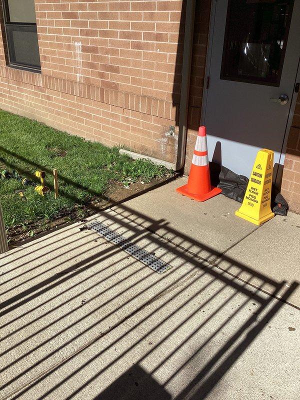 Relocated exterior drain at church front entrance to redirect water flow and prevent building intrusion. The existing drainage system was inadequate, allowing water to pool near the doorway and potentially enter the facility. Assessed the site conditions, including concrete walkway configuration and grade around the entrance area. Excavated and repositioned the drain to a more effective location that captures water runoff before it reaches the building threshold. Completed installation with proper slope and drainage pathway to ensure water is diverted away from the structure, protecting the interior from moisture damage.
