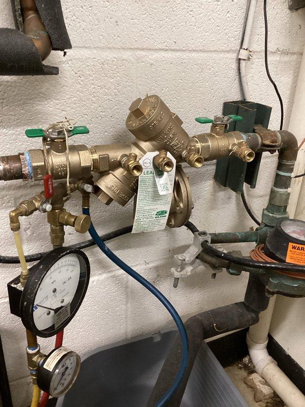 Replaced one 1-inch brass backflow prevention device on the building's main water supply line. Installed new reduced pressure zone (RPZ) assembly with dual green-handled ball valves for isolation and system maintenance. Connected pressure gauge with brass fittings to monitor differential pressure across the backflow preventer. Configured blue test port tubing for required annual testing and certification. Mounted all components securely to wall and verified proper orientation of the backflow device. Tested system operation, confirmed all valves function correctly, and ensured no leaks at compression joints or threaded connections.