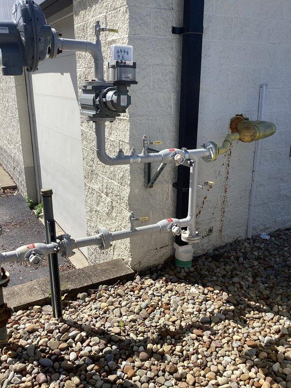 Responded to commercial gas line service call requiring flange replacement. Upon arrival, inspected existing outdoor gas line assembly mounted on building exterior and identified severely weathered and corroded brass flange connection showing significant oxidation and green patina buildup. The deteriorated flange posed potential safety concerns and required replacement with proper specification component. Assessed the complete gas line configuration including associated piping, valving, and support systems to ensure compatibility with replacement flange. Documented existing installation conditions through photographs showing the corroded flange connection, mounting hardware, and surrounding utility infrastructure. Provided proper flange component suitable for the natural gas application to restore safe and code-compliant operation of the commercial gas line system.