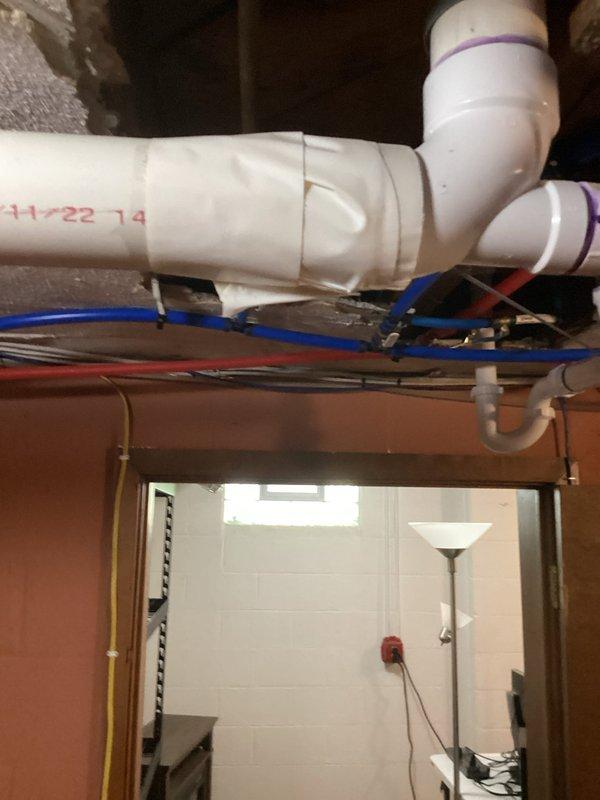 Performed diagnostic inspection of basement plumbing system to assess severely deteriorated cast iron drain stack. Found lower portion of main stack in basement had rusted through to the point of active liquid seepage, while upper portions of drain system had been previously replaced with PVC. Documented existing conditions with photographs showing corroded cast iron piping, current PVC drainage lines with proper purple-primed connections, and basement utility area layout. Provided quote for complete replacement of remaining cast iron stack section with PVC to match existing updated drain system and prevent further water damage to basement area.