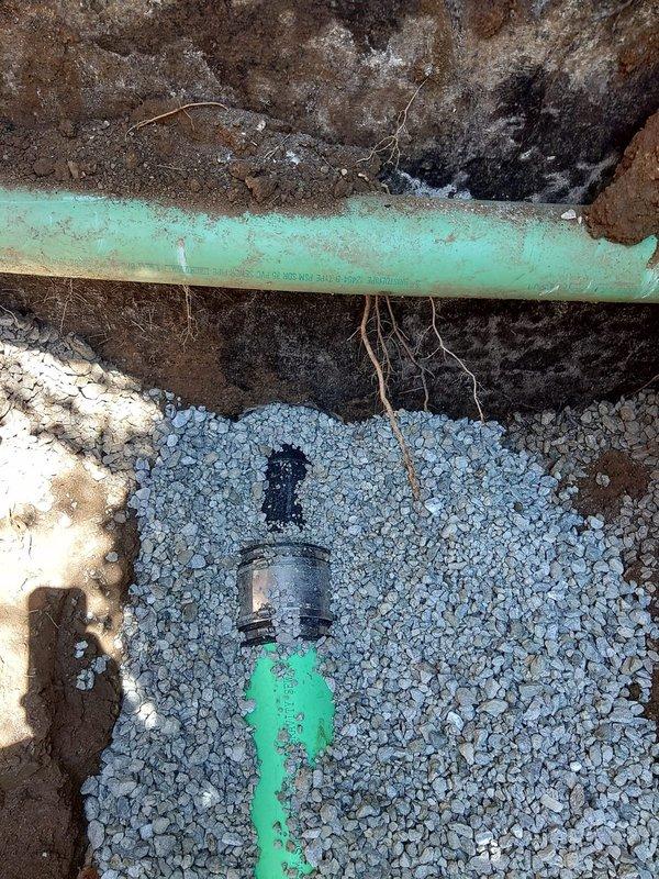 Excavated and exposed damaged sanitary sewer line, removed deteriorated section, and installed new green PVC sewer pipe with proper metallic coupling connections. Backfilled excavation with crushed stone bedding for drainage and stability, ensuring proper pipe support and grade for optimal wastewater flow.