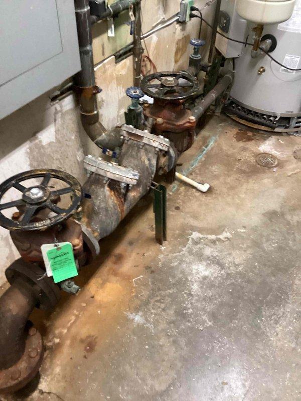Returned to site to obtain measurements of existing backflow prevention assembly for replacement planning. The current system, located in the mechanical room, shows significant age-related deterioration with heavy rust and corrosion present on valves, piping connections, and fittings throughout the assembly. Documented measurements and photographed the existing backflow device configuration, including gate valve positions, pipe routing, and connection points to facilitate accurate sizing and procurement of replacement equipment.