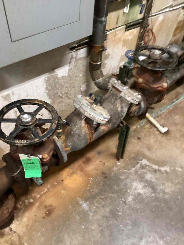 Returned to site to obtain measurements of existing backflow prevention assembly for replacement planning. The current system, located in the mechanical room, shows significant age-related deterioration with heavy rust and corrosion present on valves, piping connections, and fittings throughout the assembly. Documented measurements and photographed the existing backflow device configuration, including gate valve positions, pipe routing, and connection points to facilitate accurate sizing and procurement of replacement equipment.