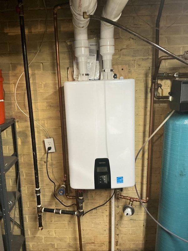 Removed existing conventional water heater and installed new wall-mounted tankless water heater unit in basement utility area. Installation included mounting unit to masonry wall, connecting copper supply and return lines with appropriate shut-off valves and fittings, installing black gas supply line with proper connections, and routing white PVC exhaust venting system through ceiling with T-junction configuration for proper combustion gas exhaust. Verified all connections for leaks, confirmed proper gas flow, tested unit operation, and ensured Energy Star certified system was functioning correctly with digital controls operational.