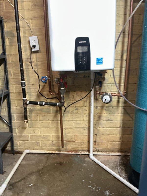 Removed existing conventional water heater and installed new wall-mounted tankless water heater unit in basement utility area. Installation included mounting unit to masonry wall, connecting copper supply and return lines with appropriate shut-off valves and fittings, installing black gas supply line with proper connections, and routing white PVC exhaust venting system through ceiling with T-junction configuration for proper combustion gas exhaust. Verified all connections for leaks, confirmed proper gas flow, tested unit operation, and ensured Energy Star certified system was functioning correctly with digital controls operational.