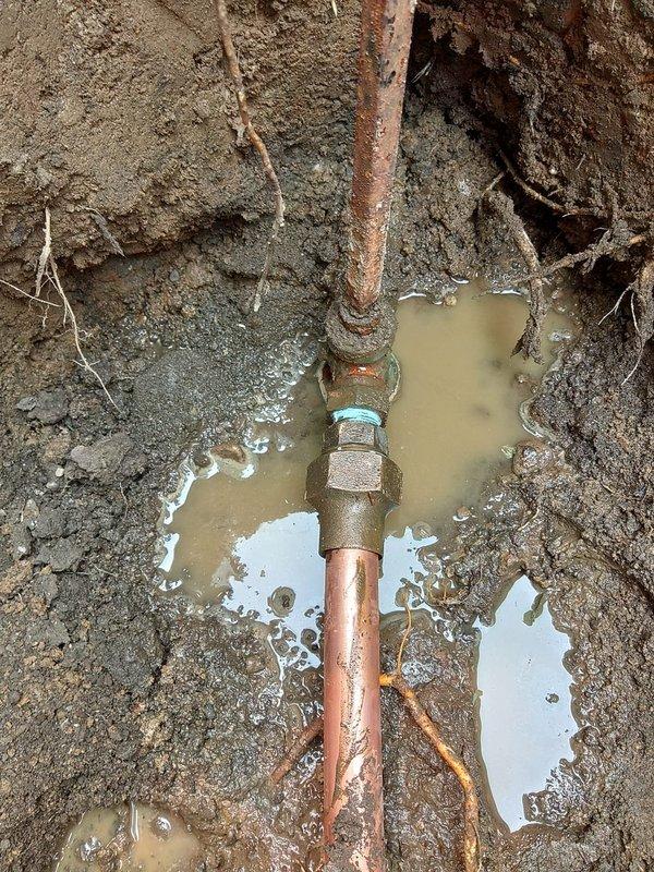 Excavated and replaced approximately 40 feet of corroded exterior water line from the meter at the curb to the home using 1" copper pipe and brass fittings. Trench was dug through the yard, extending under one sidewalk section which required slab removal for access. The existing line showed significant corrosion and deterioration at connection points, with heavy rust buildup and mineral deposits visible on the old piping. New copper line was installed along the trench bottom, properly fitted and connected at the meter junction. Excavated soil was staged alongside the trench for backfilling upon inspection approval. Work was performed under permit with municipal inspection scheduled as required.