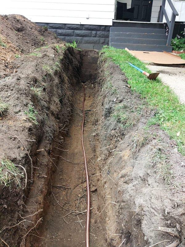 Excavated and replaced approximately 40 feet of corroded exterior water line from the meter at the curb to the home using 1" copper pipe and brass fittings. Trench was dug through the yard, extending under one sidewalk section which required slab removal for access. The existing line showed significant corrosion and deterioration at connection points, with heavy rust buildup and mineral deposits visible on the old piping. New copper line was installed along the trench bottom, properly fitted and connected at the meter junction. Excavated soil was staged alongside the trench for backfilling upon inspection approval. Work was performed under permit with municipal inspection scheduled as required.