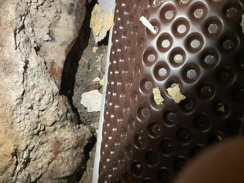 Conducted on-site assessment of exposed flood drain system in basement area requiring repair. Inspected white PVC drainage piping running horizontally through the space, along with associated heating register components and concrete surfaces showing signs of moisture exposure and deterioration. Documented existing conditions including deteriorated insulation material with significant cracking and flaking, perforated metal HVAC components with visible water staining and mineral deposits, and concrete block walls displaying efflorescence. Provided detailed photographic documentation of the flood drain system and surrounding infrastructure to prepare comprehensive repair estimate for the exposed drainage work as requested.