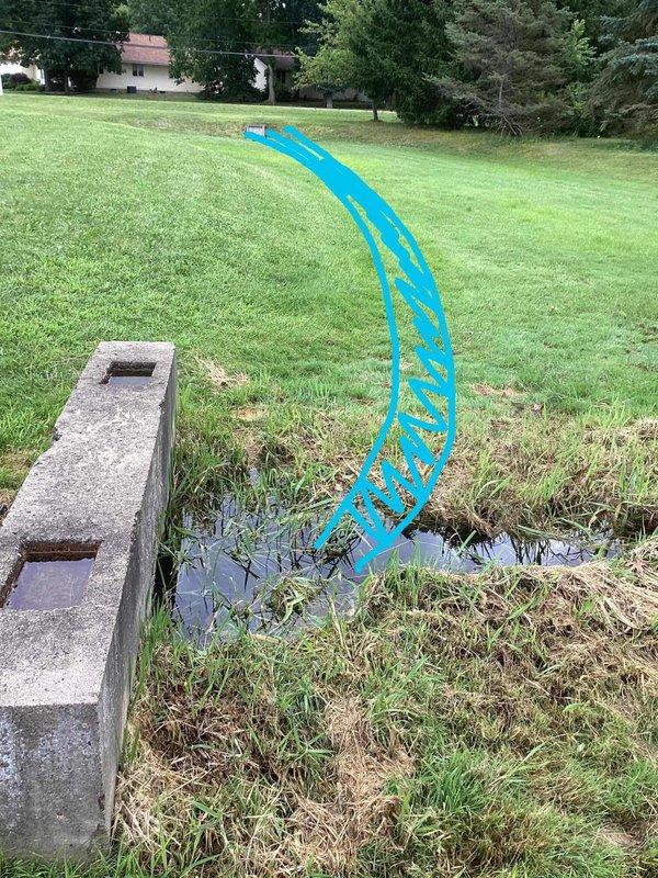 Responded to commercial property for backed-up downspouts at front of building. Upon arrival, inspected ground water drainage system and located catch basin with metal grate covering. Assessed drainage structure showing signs of age and weathering, with water pooling evident in surrounding lawn area. Documented existing conditions including catch basin dimensions and drainage flow patterns. Cleared obstruction from downspout drainage system to restore proper water flow and prevent further backup issues.