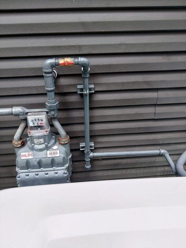 Installed 10 feet of natural gas piping to an exterior tap location, connecting to the existing gas meter assembly mounted on the building's exterior wall. The installation included proper routing of gray PVC piping with secure mounting brackets, integration with the existing meter configuration featuring a red shut-off valve, and copper flexible connectors at the meter connections to ensure code-compliant gas delivery to the designated tap point.