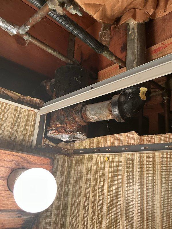 Responded to upstairs bathroom sink drainage issue with secondary leak observed in downstairs area. Upon inspection, discovered severely corroded plumbing infrastructure in older home with compromised metal pipes and fittings showing extensive rust and oxidation. Documented existing conditions of deteriorated drainage system, including aged basement plumbing components requiring replacement parts and materials. Two affected drain lines identified with visible corrosion at connection points and pipe assemblies, indicating long-term moisture exposure and compromised structural integrity of plumbing system.