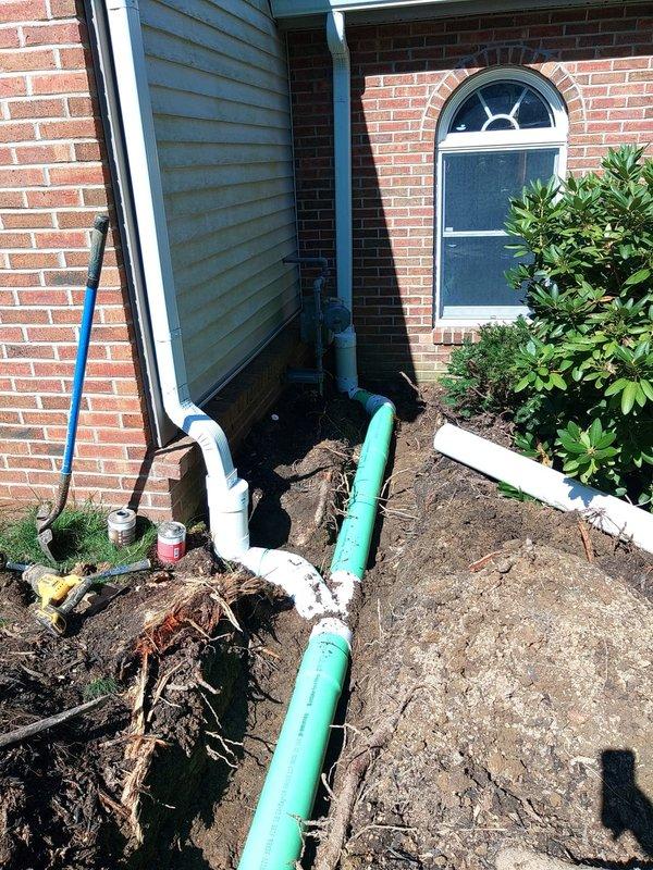 # Downspout and Ground Water Drainage System Replacement

Replaced deteriorated downspouts and installed new ground water drainage system on the front exterior of residential brick units. Work included excavation along the foundation, installation of white PVC downspout extensions mounted to brick exterior, and underground drainage piping utilizing turquoise and white PVC components with proper elbows and fittings to direct water away from the building foundation. Backfilled excavated areas and restored ground surface upon completion.